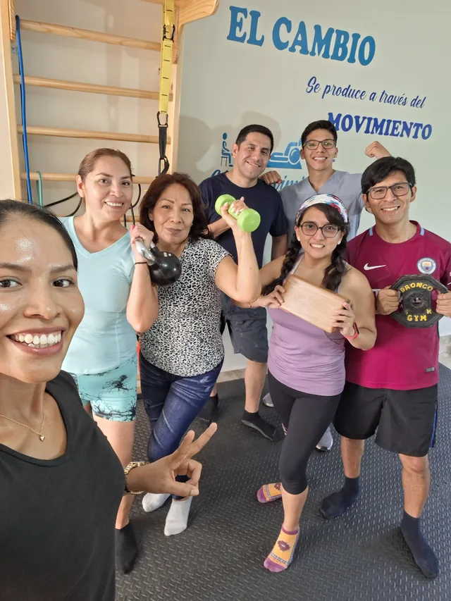 Pacientes y fisioterapeutas sonríen juntos bajo el mural El cambio se produce a través del movimiento
